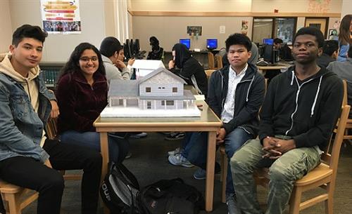 4 students next to a model house